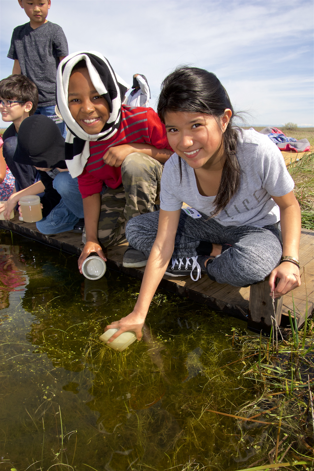 Two students collecting pond water samples during an outdoor learning activity.